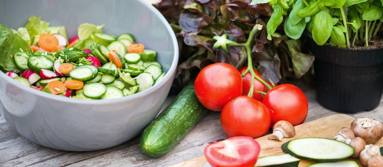 Salt in einer weißen Schüssel. Daneben liegen Tomaten und eine Gurke.